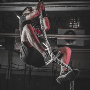 A determined man climbing a rope in an indoor gym setting, showcasing strength and fitness.